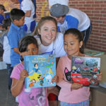 elementary students receiving book from female athlete