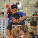 male athlete signing book for boy at elementary school