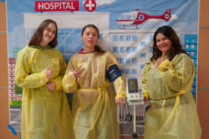 Three female students in yellow scrub gowns smile for the posed photo.