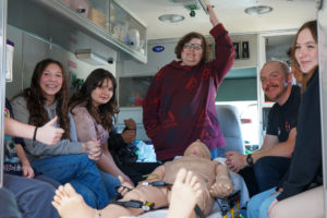 Several students sit inside an ambulance.