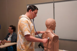 A student uses a stethoscope to listen to a model's "heartbeat" at Scrub Camp.