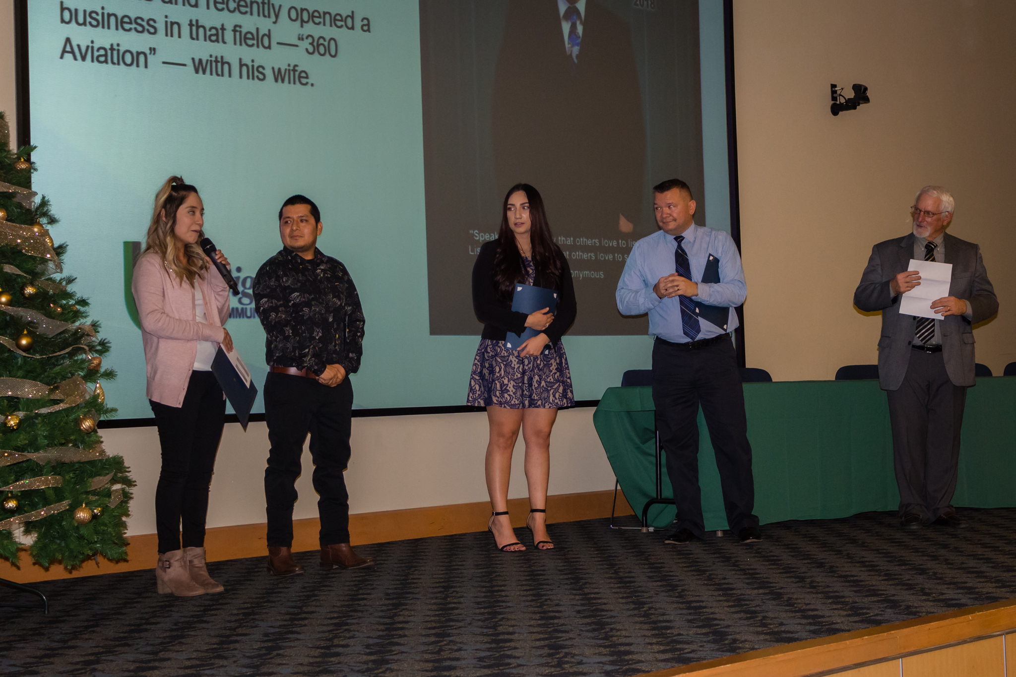 female student speaking into a microphone with three other students on stage