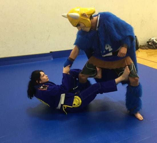 Jiu-Jitsu club member rolling with Viking Mascot on mats