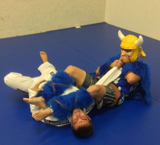 Jiu-Jitsu club member rolling with Viking Mascot on mats