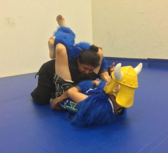 Jiu-Jitsu club member rolling with Viking Mascot on mats