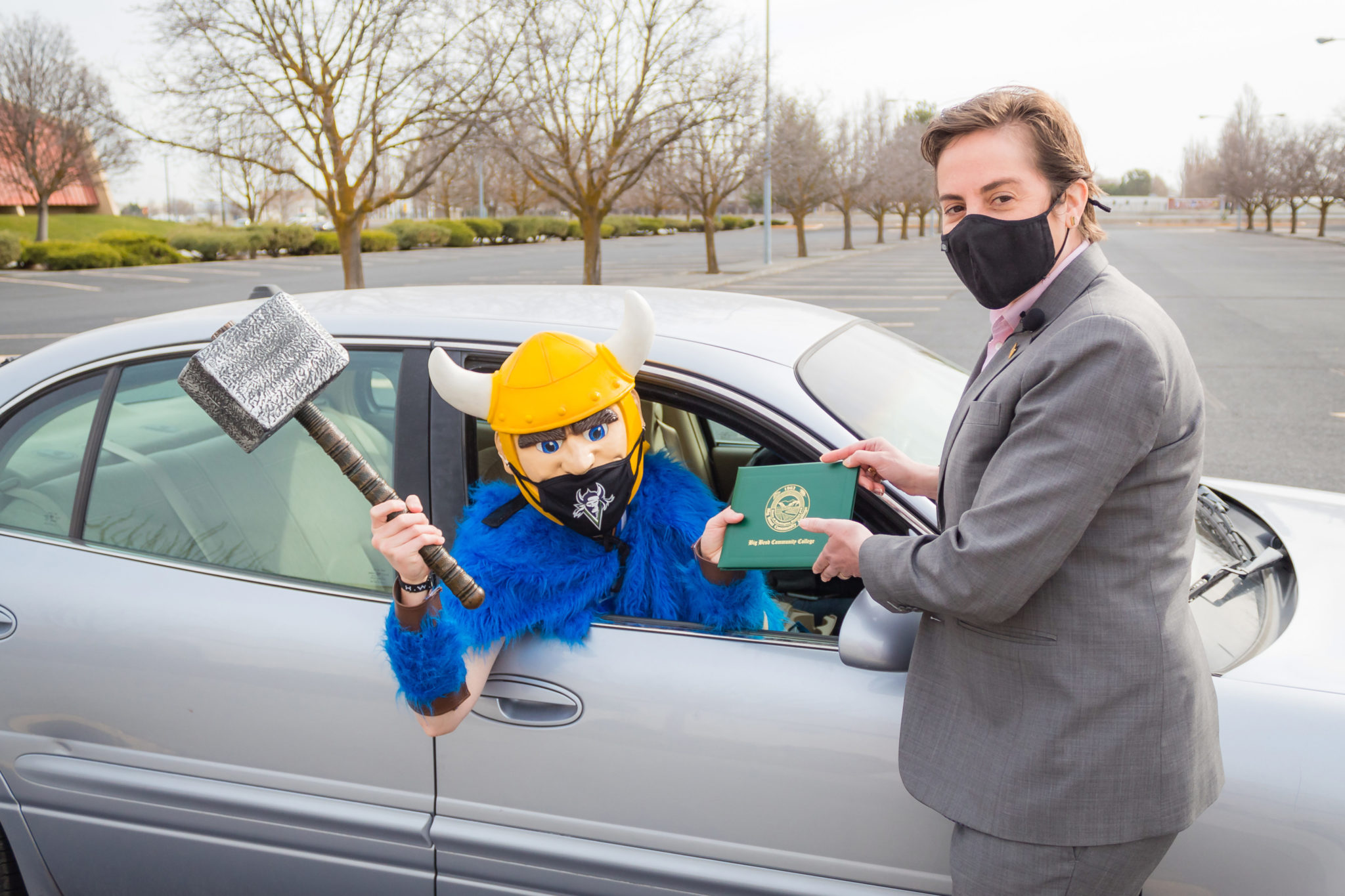 BBCC President Sara Thompson Tweedy handing Thor the mascot a diploma while Thor sits in the car