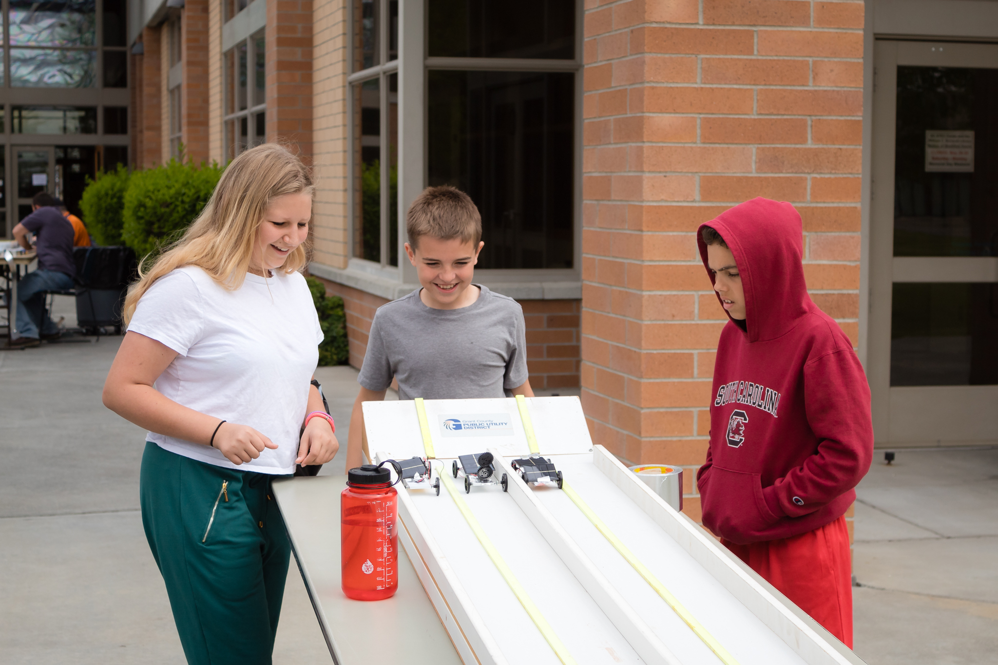 Three children look at three solar cars moving down a track.