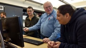 Teacher and two students standing by computer